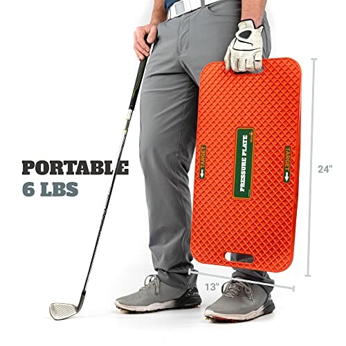 Person holding an orange portable golf swing trainer mat with a golf club.